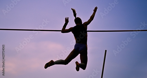 A female pole vaulter (silhouette) jumping with a beautiful sky in the background. Track and field athlete. Young woman pole-vaulting. Pole vault competition