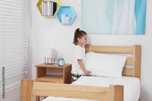 Cute girl changing bed linens in children room