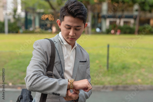 A young male employee on the go double checks the time on his golden watch. Commuting by foot to work.