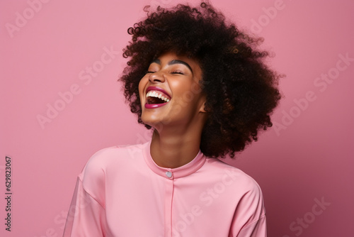 laughing young black woman with afro wearing pink on a pink background, studio portrait