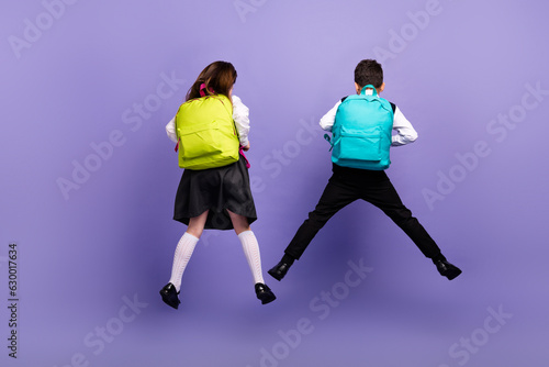 Back rear photo of two schoolkids jumping wear new backpack on school discounts isolated purple color background
