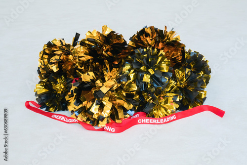 Gold and black pompoms with a red cheerleading ribbon on a white practice mat