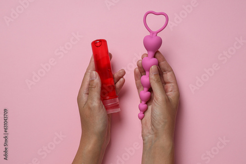 Lubricant with anal balls in hands on pink background