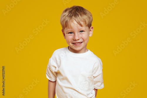 Happy little blonde male kid boy in white tshirt laughing at camera against orange background