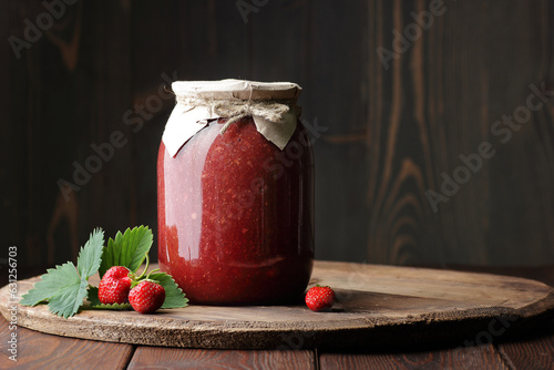 Strawberry jam in glass can with fresh berry and leaf on wood and rustic background, cottagecore aesthetic, copy space, batch cooking, sustainable living, zero waste storage concept