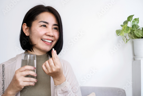 healthy Asian woman taking probiotic supplement pill with a glass of water