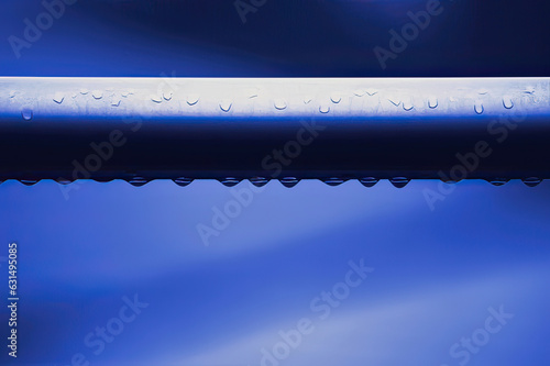Water drops bead on a metal pipe and go to drip, blue montone hue
