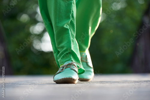A woman in green trousers and moccasins walks along the road in summer