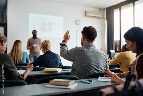 Back view of older student raising his hand to answer teacher's question during education training class.