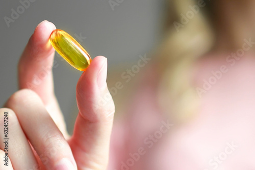 Close-up of a yellow capsule of omega-3 nutritional supplement or fish oil or vitamin D3 in a woman's palm