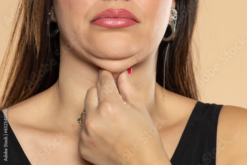 Young woman touches her double chin on beige background, closeup. Front view