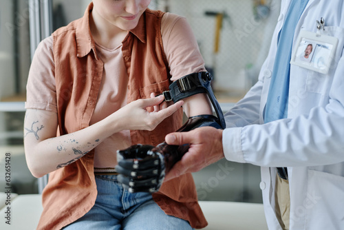 Closeup of doctor consulting young woman and fitting prosthetic arm in orthology clinic