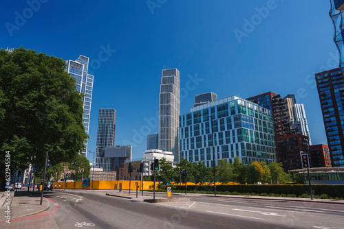 Empty road by modern buildings in capital city. Highway surrounded by trees with clear blue sky in background. View of downtown district during sunny day.