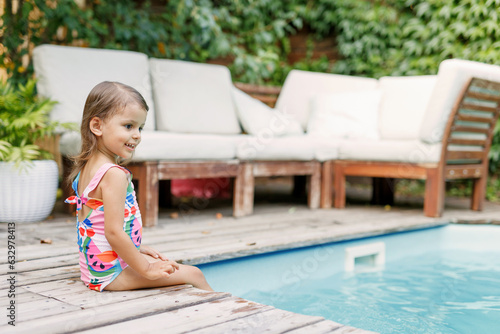 Funny cute girl on summer vacation. The child has fun near the pool. Cute baby girl in a colorful swimsuit and sunglasses is resting.