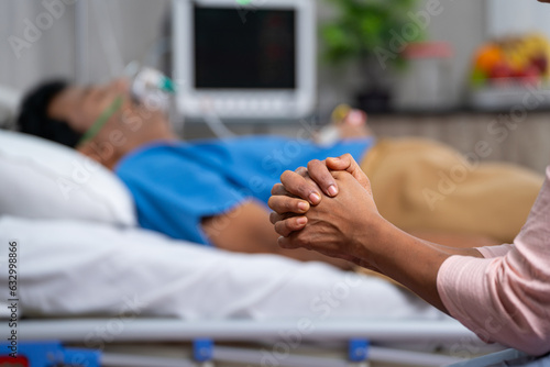 Close up shot of wife hands or family hands praying for admitted fathers health recovery at hospital near bed - concept of family caring, Emotional Bonding and togetherness