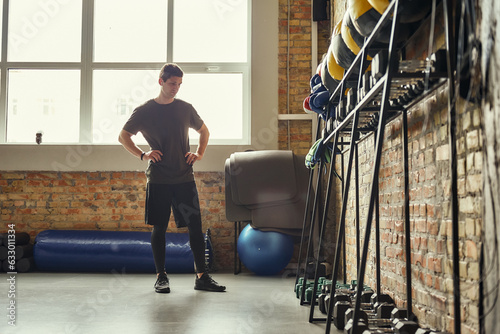 Ready for workout. Confident young man is looking at sport equipment while exercising at gym.