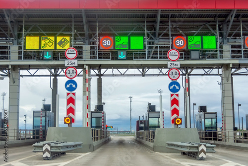 View gate for cars at the entrance to the toll road, limited by the barrier. Cashless payment transponder, speed limit signs.