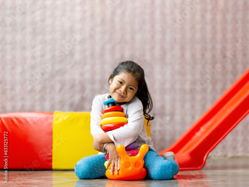 Niña latina feliz jugando con pequeña torre de aros de colores. Entretenimiento interior. Motricidad