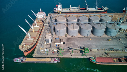 Loading grain into holds of sea cargo vessel in seaport from silos of grain storage. Bunkering of dry cargo ship with grain. Aerial top view