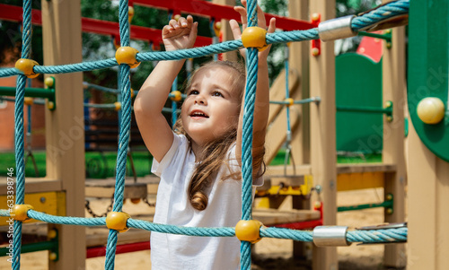 A child climbs up an alpine grid in a park on a playground on summer day. children's playground in a public park, entertainment and recreation for children