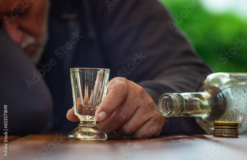 Ein Mann schläft betrunken an einem Tisch. Eine leere Flasche und ein Schnapsglas sind vor ihm.