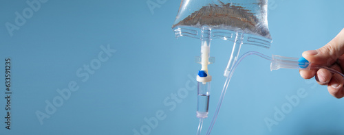 Male hand checking an intravenous drip on the blue background.