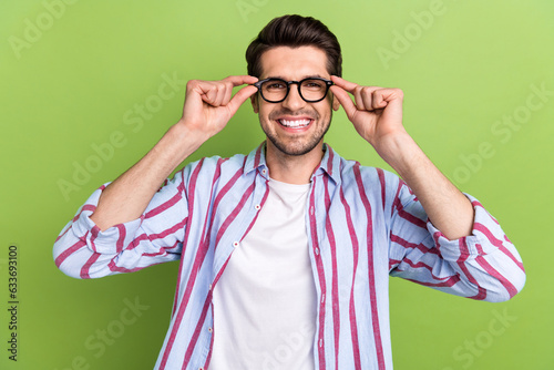 Portrait of satisfied pleasant person with brunet hair wear stylish clothes fingers touching glasses isolated on green color background