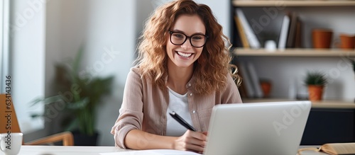 Smiling woman at desk using laptop and notebook studying online at home