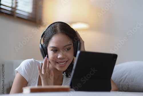 Young African woman holding tablet with earphones sitting on sofa at home.