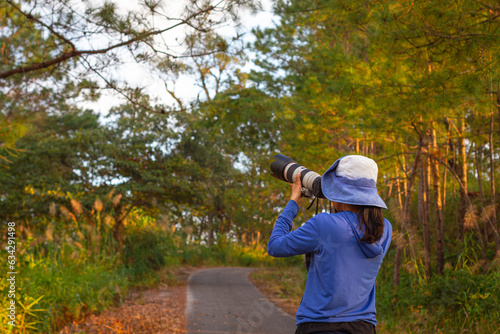 Cheerful female photographer stands with a car on the side of the road taking a picture with a digital camera in the mountains. Travel and active living and tourism concept.