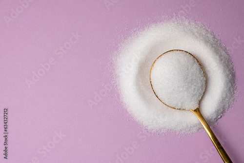 Erythritol in a golden spoon on a lilac background. Diet, healthy food concept.