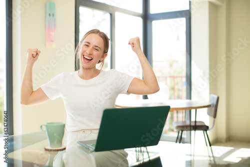 caucasian pretty woman with a laptop feeling happy, satisfied and powerful, flexing fit and muscular biceps, looking strong after the gym