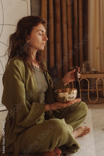 Woman playing on Tibetan singing bowl while sitting on yoga mat. Vintage tonned. Soft focus blurred and noise effect