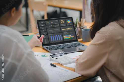 Two businesspeople or an accountant team are analyzing data charts, graphs, and a dashboard on a laptop screen in order to prepare a statistical report and discuss financial data in an office.