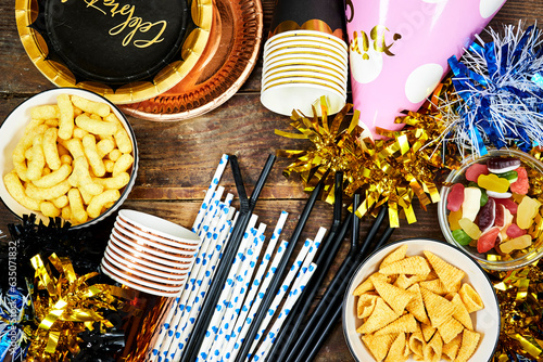 birthday or christmas, new year's party concept, paper plate with card celebrate text and disposable cup, straws and colorful with different chips and candies, pink hat tinsel on wooden table