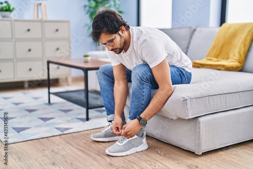 Young hispanic man tying shoe at home