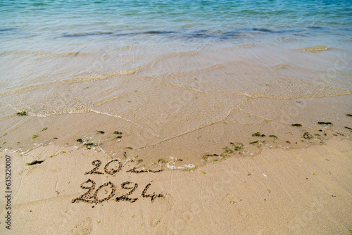 Bonne et heureuse année 2024, élégante carte de voeu montrant la fin de 2023 et le passage à 2024 sur le sable d'une plage et mer turquoise. Slogan à ajouter