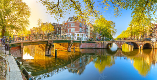 Panoramic view of Amsterdam in the morning sun. Traditional old houses, bridges and mirror water with reflection. Beautiful morning in Amsterdam.