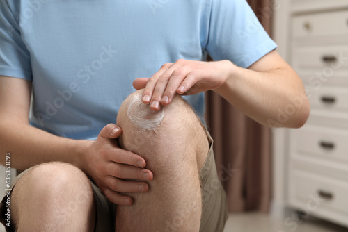 Man applying ointment onto his knee indoors, closeup