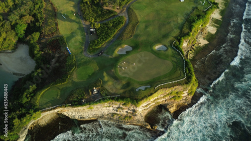 Drone footage of a group of people playing golf at a country club perched on a cliff by the ocean. Green golf course on the coast, people play golf.