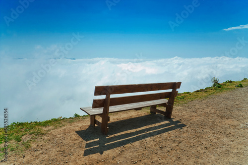 Bench without people on precipice above the clouds.