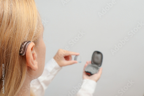 Blond woman Inserts Hearing Aid on ear at home. Deafness treatment, hearing solutions. Deaf woman wearing hearing aid. Digital hearing aid in woman's ear.