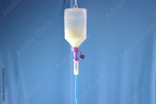 Enteral nutrition diet bottle hanging and infusing enteral diet throughout an infusion set. Blue background