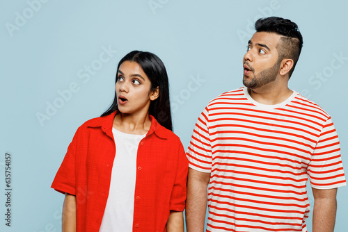 Young shocked surprised astonished couple two friends family Indian man woman wearing red casual clothes t-shirts look aside on area together isolated on pastel plain light blue cyan color background.