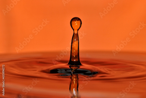 Water droplet impact water surface and make lovely water column. Water drop splash abstraction on blurred orange surface. 