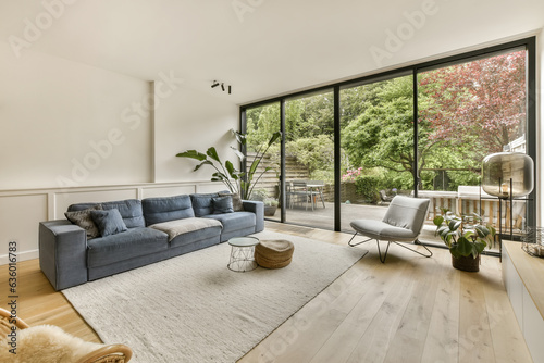 a living room with wood flooring and large windows looking out onto the trees in the backyard area is bright