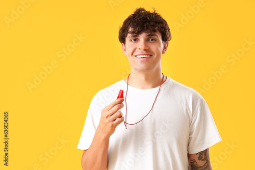 Male lifeguard with whistle on yellow background