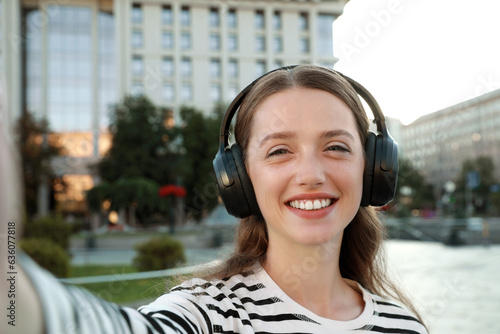 Portrait of smiling woman in headphones taking selfie on city street