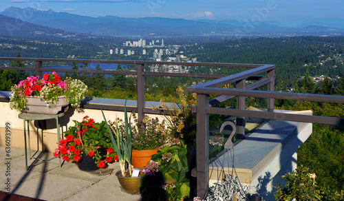 Bright summer flowers in planters on patio overlooking Burrard Inlet and Fraser Valley with mountains in silhouette in background