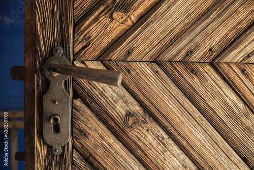 zdobione brązowe drzwi drewniane z metalową kutą klamką oraz zamkiem.